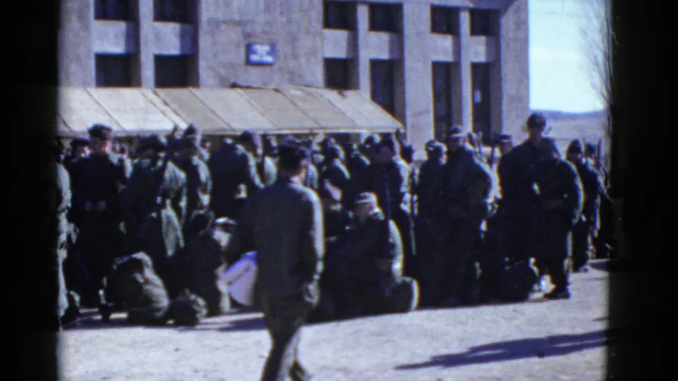 A passerby crosses in front of uniformed men waiting with bags outside a San Francisco building in early-1950s home-movie footage.