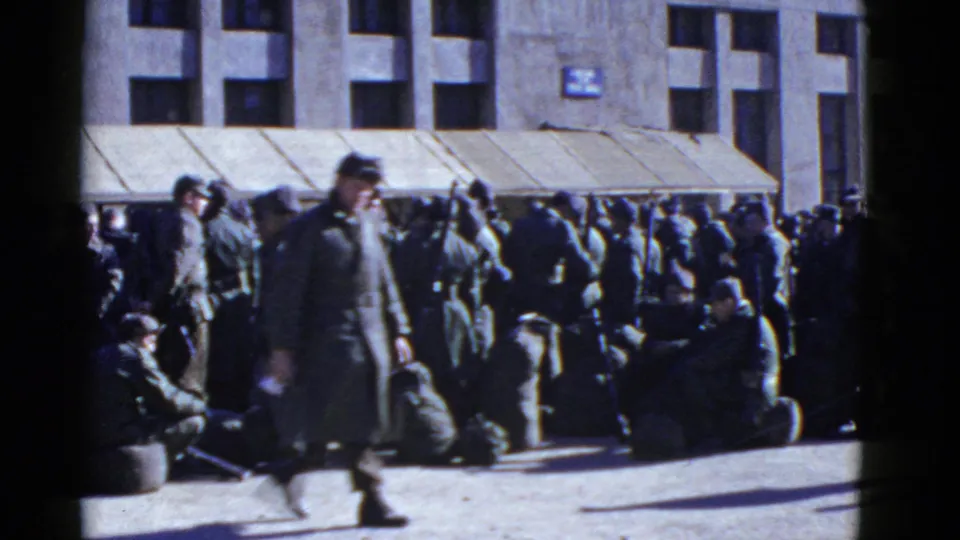 A long-coated figure moves across the foreground while uniformed men wait with gear outside the San Francisco building.