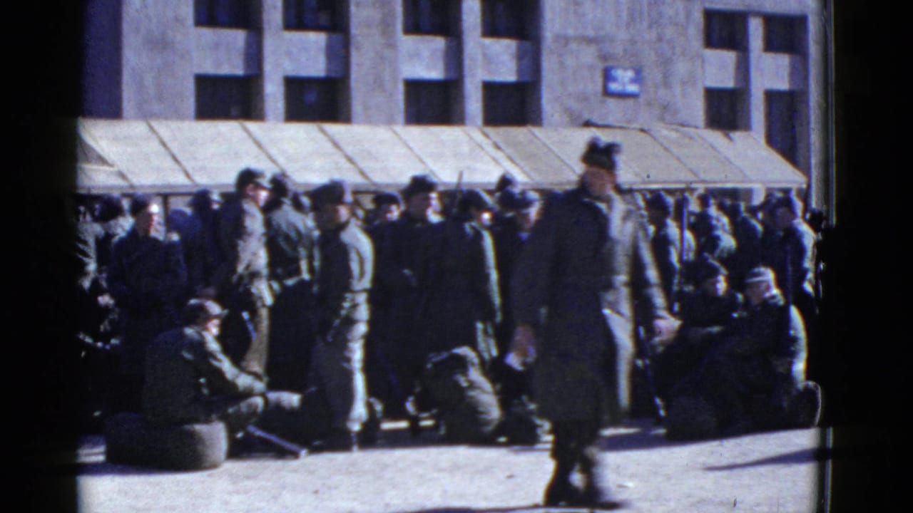 1950s home-movie frame of uniformed men gathered with bags outside a San Francisco building with an awning.