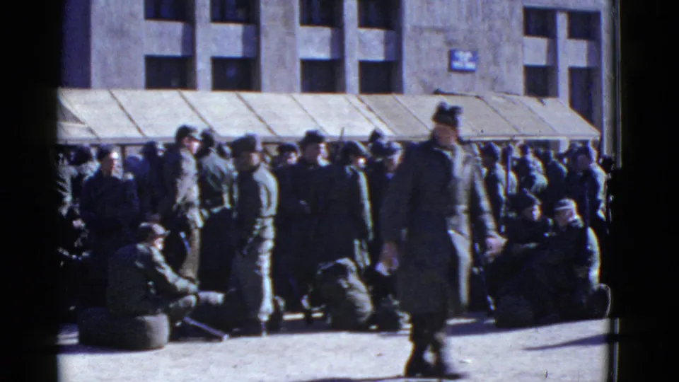 1950s home-movie frame of uniformed men gathered with bags outside a San Francisco building with an awning.