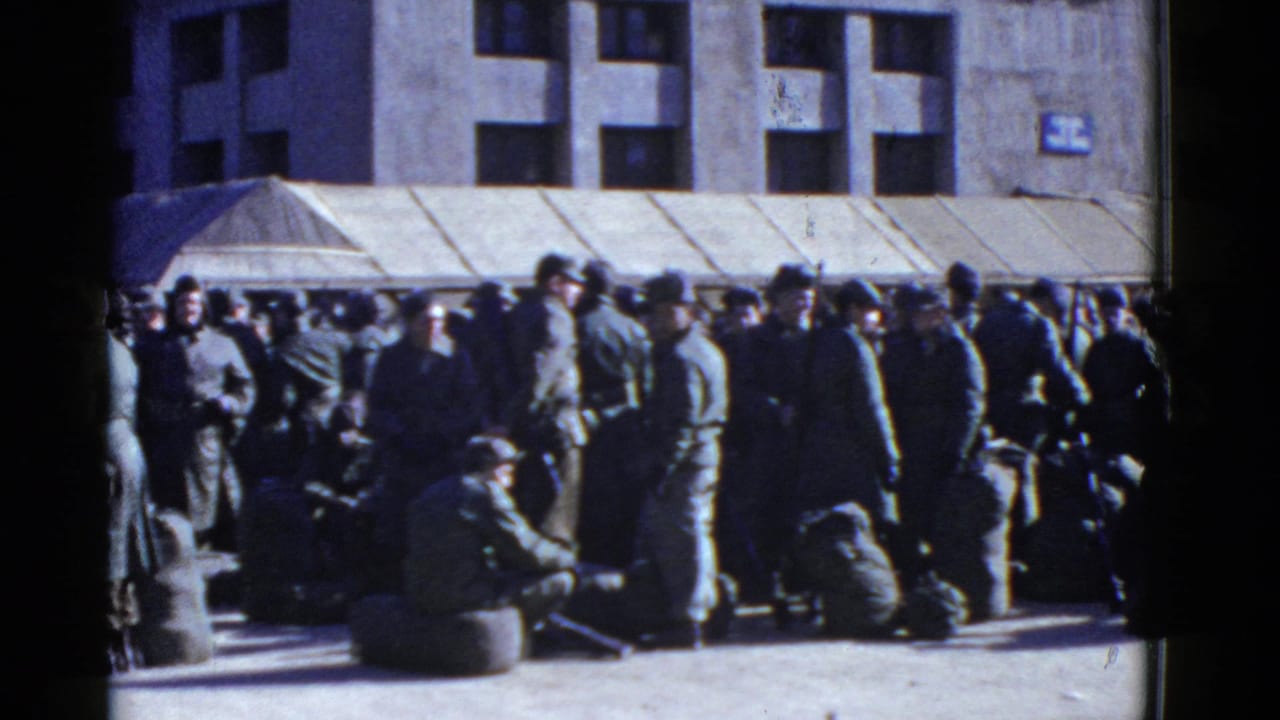 Uniformed soldiers gather in San Francisco in a 1950s 8mm frame, with bags on the ground near a building awning.