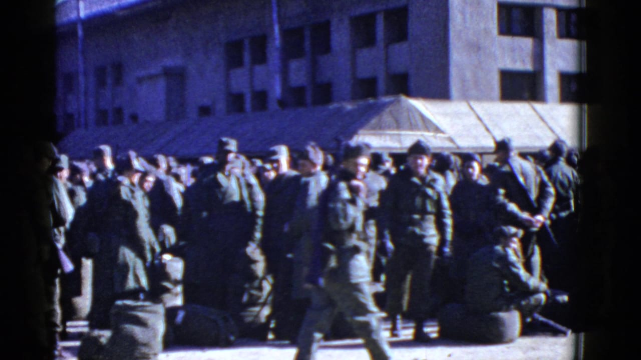 Soldiers in uniform gather outside a large building with bags on the pavement.