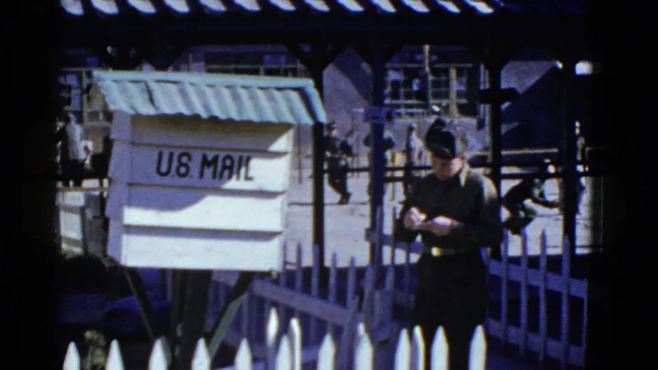 1950s San Francisco 8mm still with U.S. Mail signage, a uniformed man, and personnel moving behind a fenced courtyard.