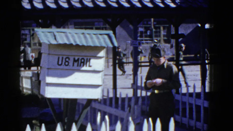 In supported 1950s San Francisco base footage, a uniformed soldier stands by a U.S. Mail box with other soldiers walking in the background.