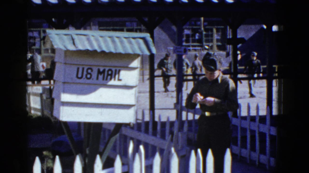 Soldier looks down at a letter near a white U.S. Mail box.