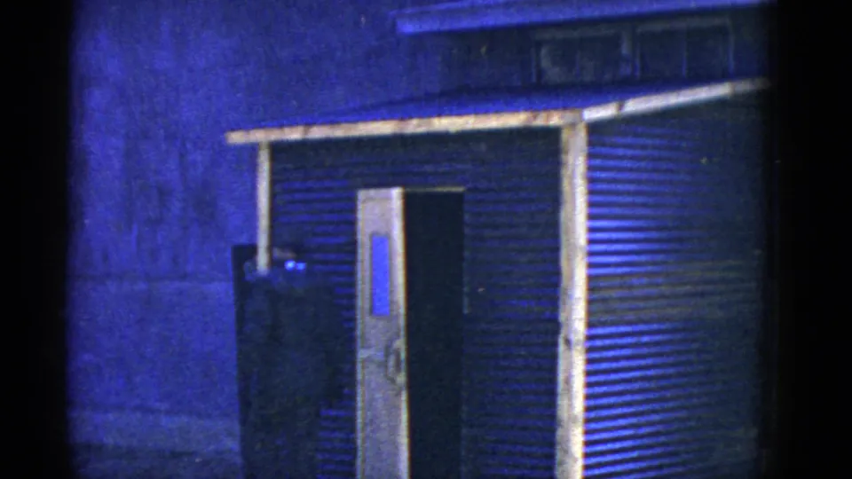 The final frame holds on a corrugated building entrance with an open door and dark interior under blue-tinted lighting.