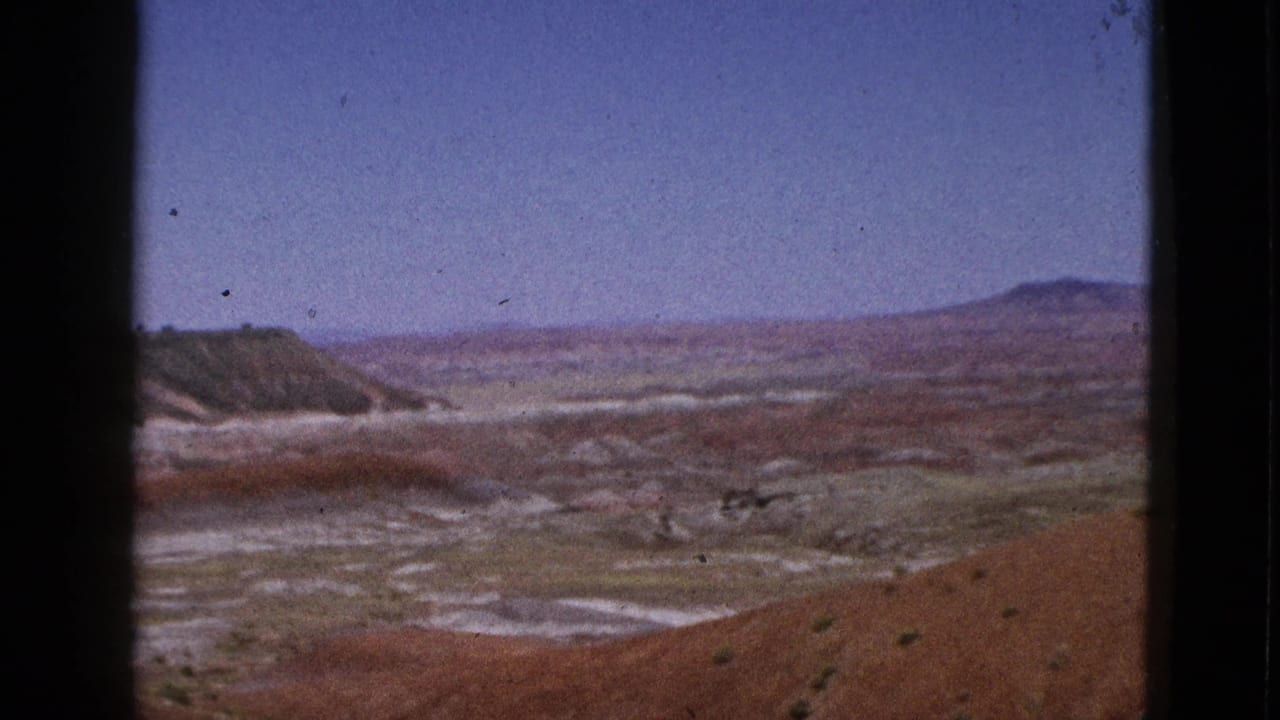 Dry basin and reddish slopes framed by dark 8mm borders, with low hills on the horizon.