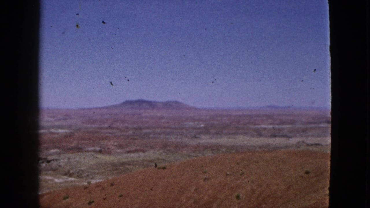 Open valley landscape with low mountains in the distance and reddish earth in the foreground.