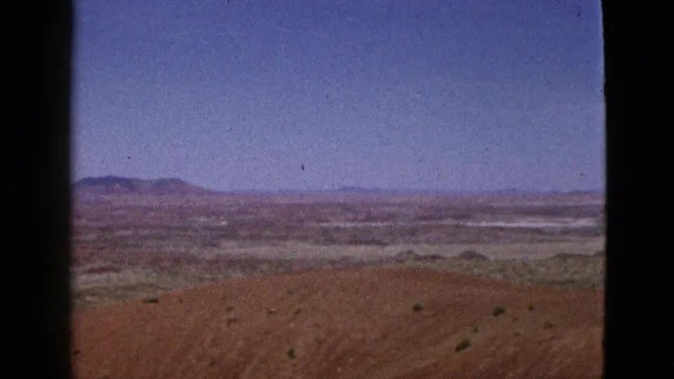1953 California travel frame showing open desert foreground, a broad valley, and distant mountains beneath clear sky.