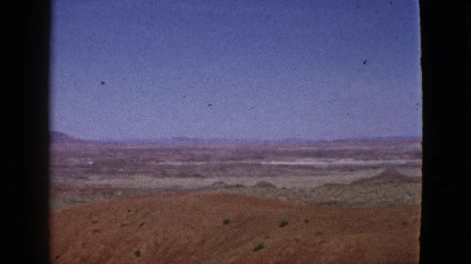 1953 California desert panorama with low shrubs, reddish soil, distant mountains, blue sky, and a dark vertical film-frame divider.