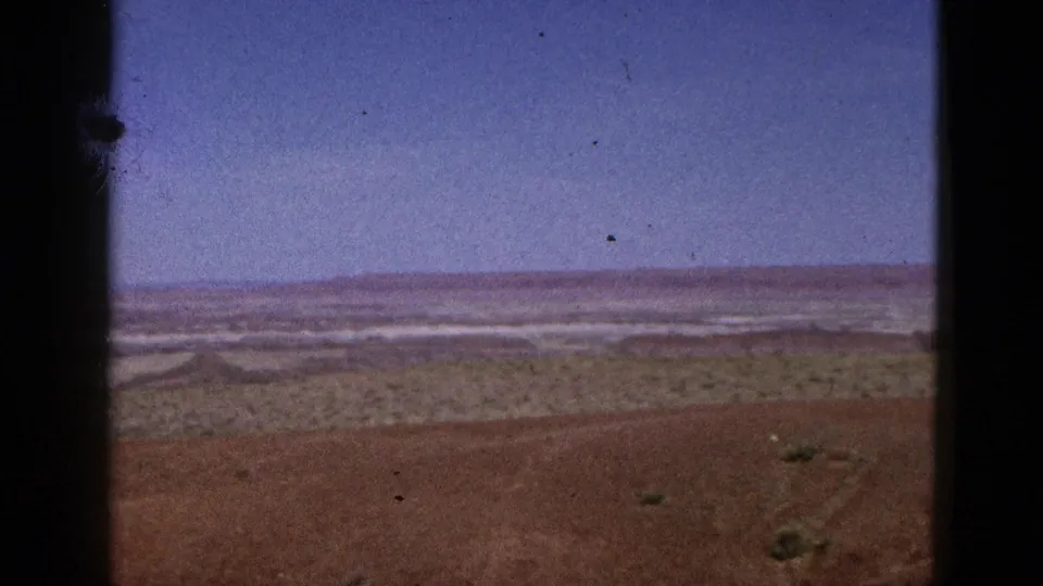 1953 California 8mm view across desert flats with scattered vegetation, pale distant ground, low hills, and visible film dust.