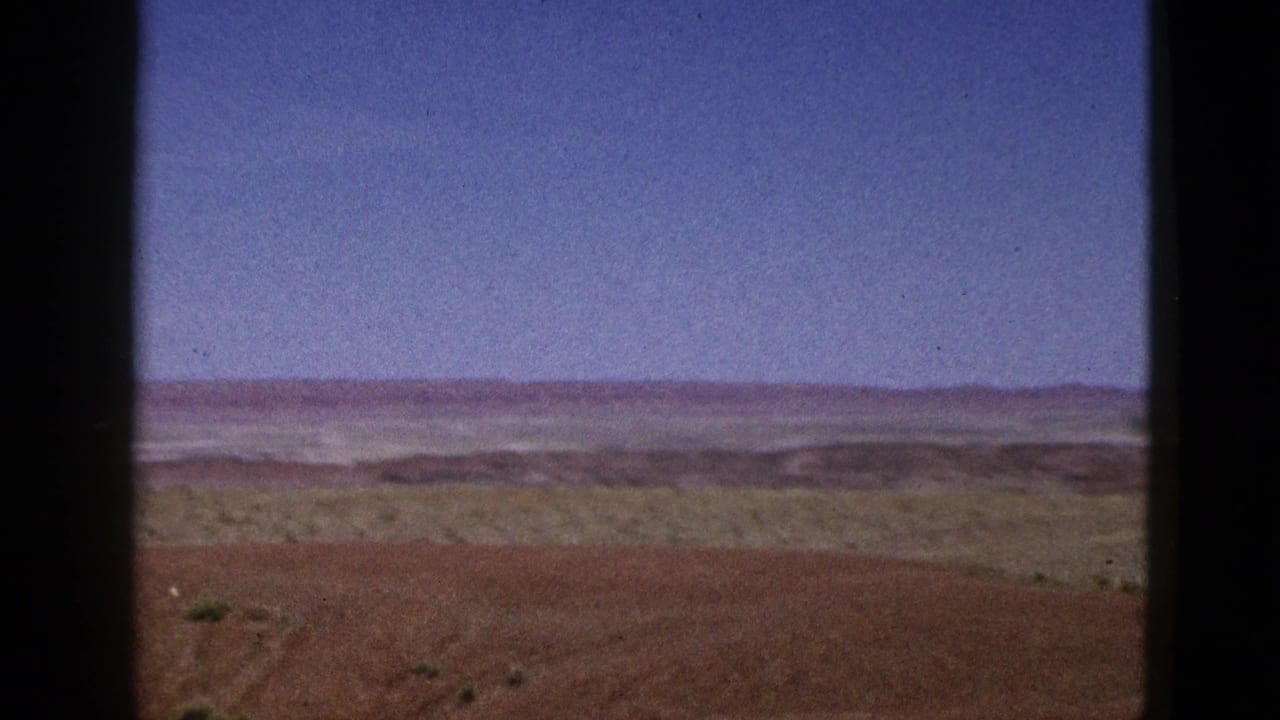 1953 California 8mm frame showing dry brown hills, sparse vegetation, distant ridgelines, and a wide blue sky.