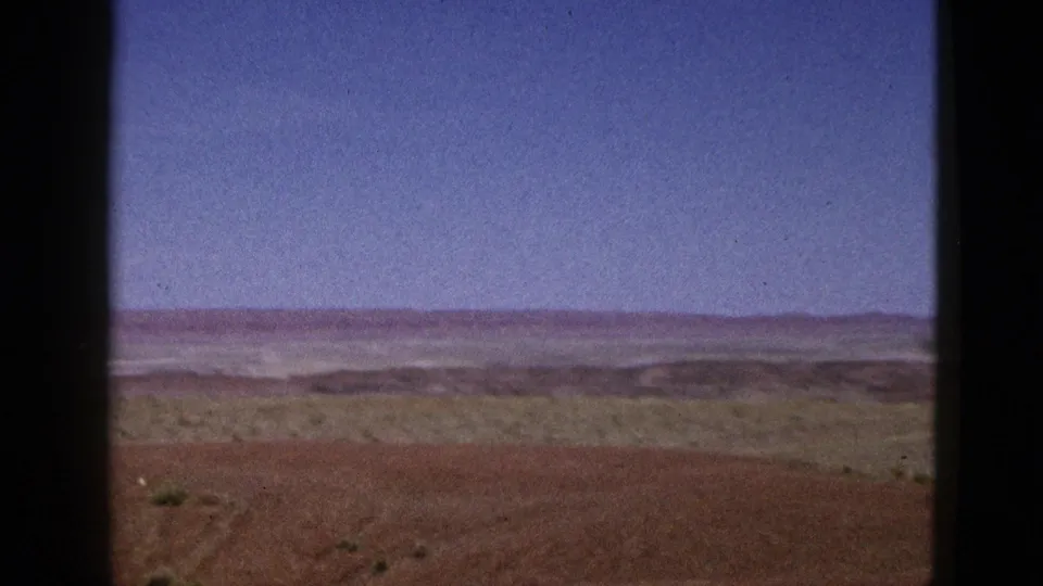 1953 California 8mm frame showing dry brown hills, sparse vegetation, distant ridgelines, and a wide blue sky.