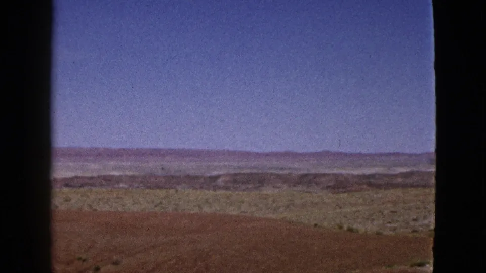 1953 California landscape frame with reddish-brown ground, low scrub, distant hills, and visible 8mm frame edge.