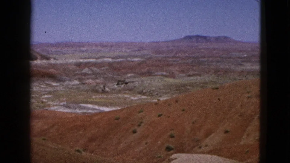 1953 California 8mm view of eroded pale washes, reddish hills, sparse brush, and a distant low mountain.