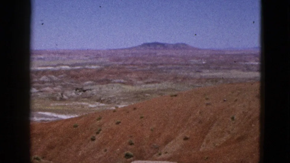 1953 California frame showing a dry ridged hillside, pale eroded channels, scattered shrubs, and a distant mountain.