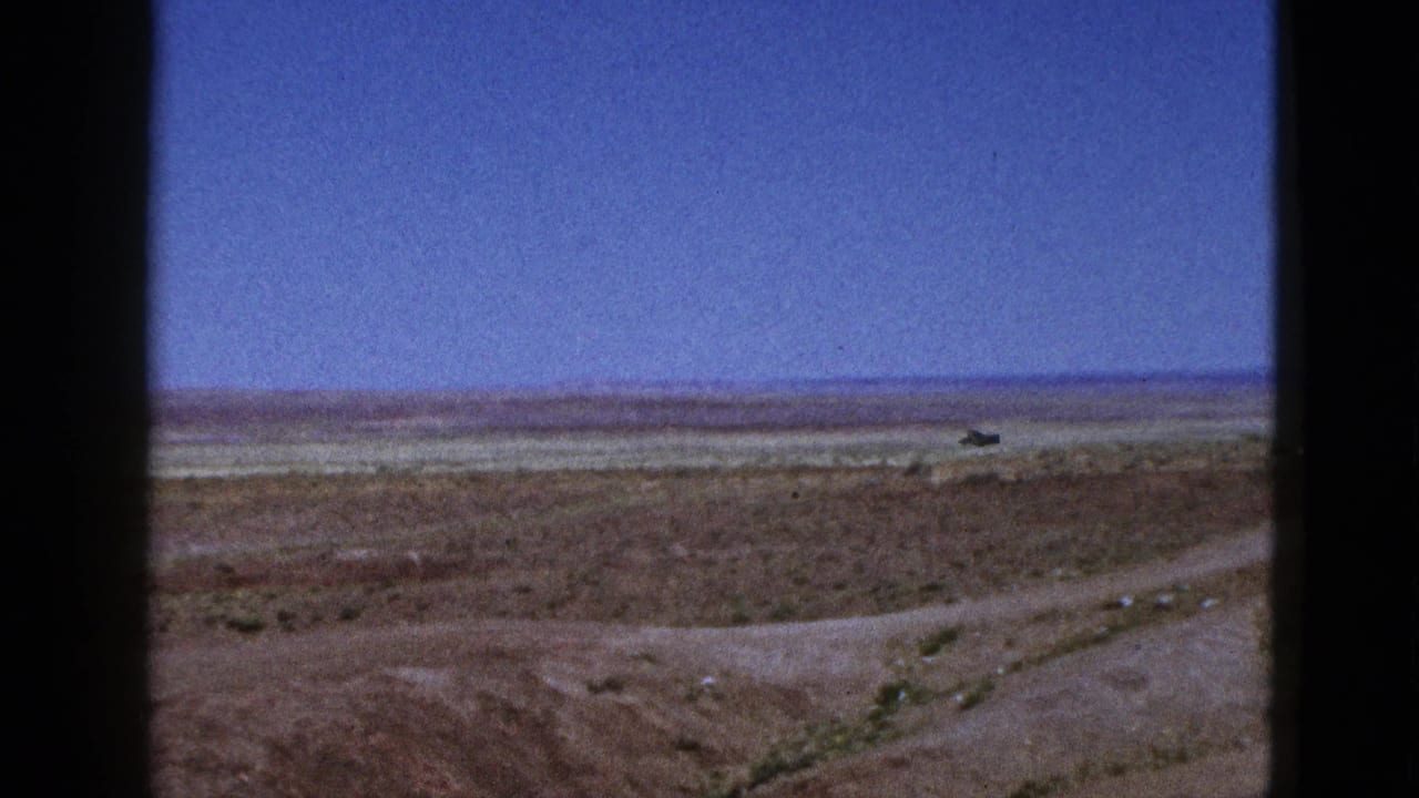 1953 California 8mm frame showing a wide desert horizon, pale graded ground, and a rough dirt track crossing the foreground.