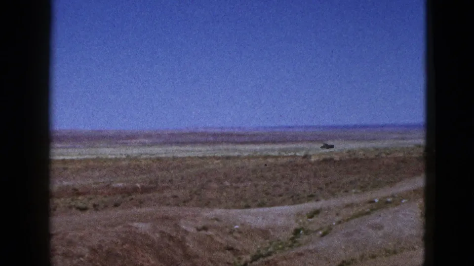 1953 California 8mm frame showing a wide desert horizon, pale graded ground, and a rough dirt track crossing the foreground.