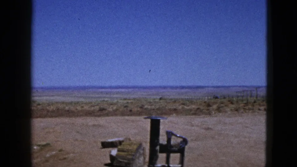 1953 California 8mm frame showing empty desert terrain, distant low hills, and a wooden object with a metal frame in the foreground.