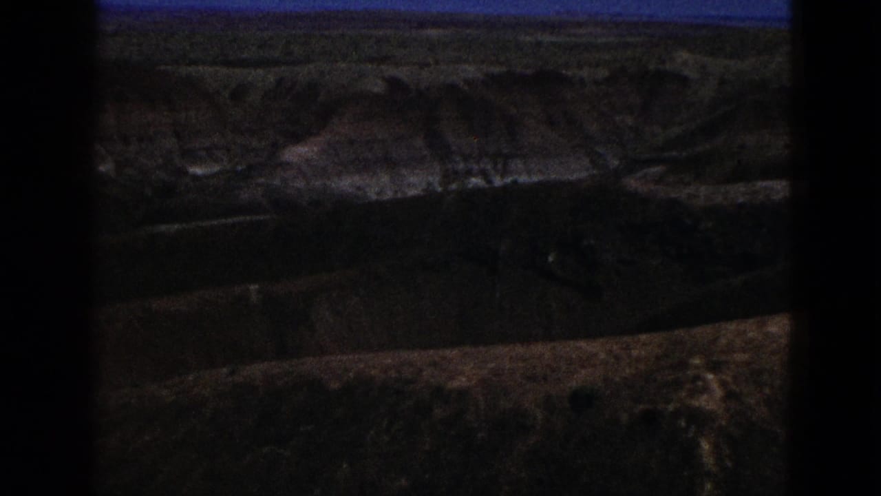 1953 California home-movie frame showing arid layered hills under blue sky, darkened by exposure and film-gate edges.