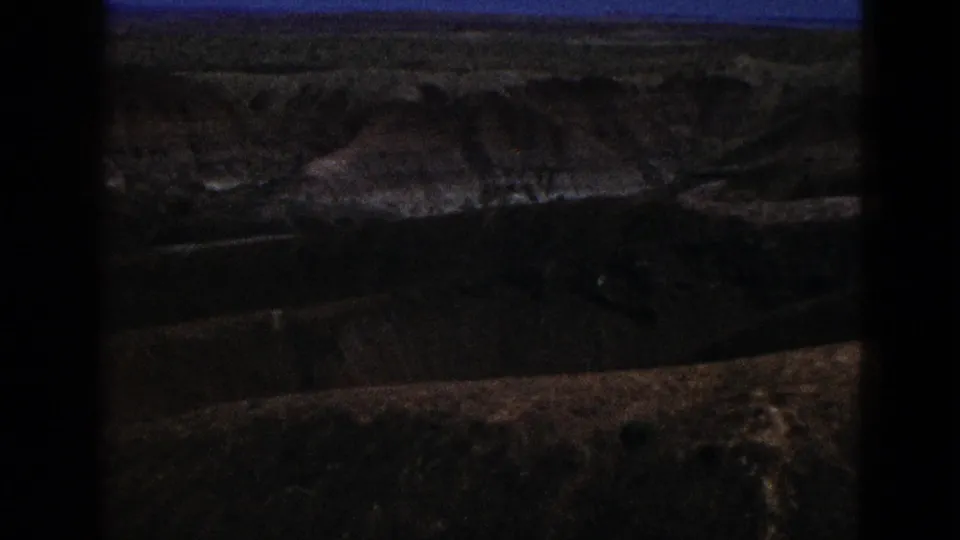 1953 California home-movie frame showing arid layered hills under blue sky, darkened by exposure and film-gate edges.