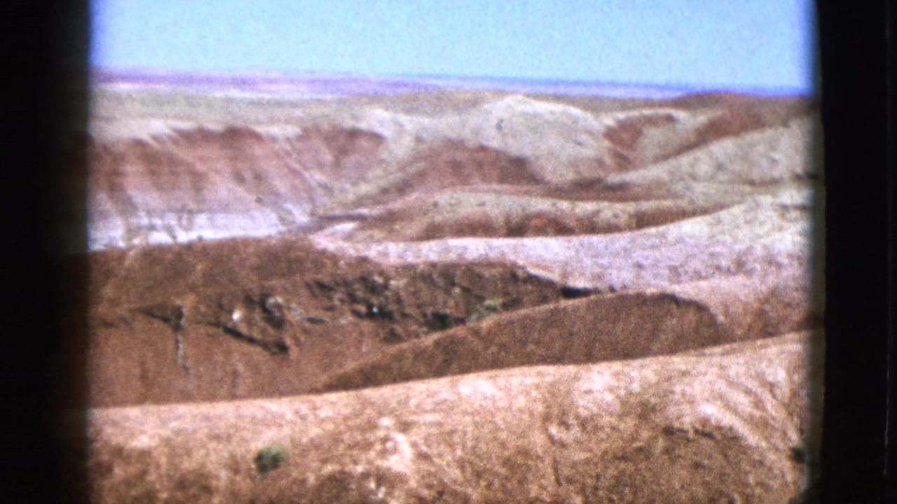 Bright view of pale and reddish dry hills beneath a clear blue sky.