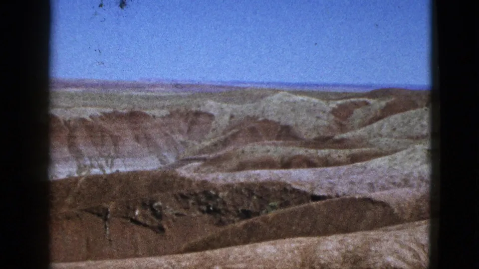 Mid-century 8mm frame from California showing dry rolling terrain, pale rock layers, and sparse vegetation.