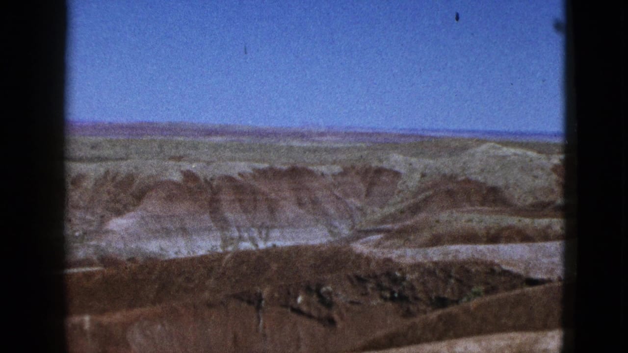 1953 California 8mm frame showing distant greenish fields, brown mesa ridges, and pale desert slopes under clear sky.