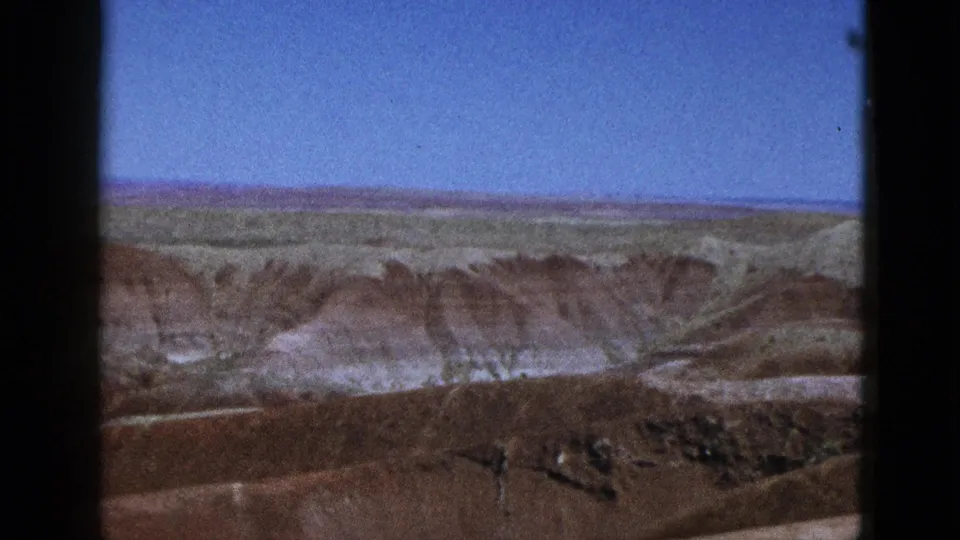 1953 California home-movie view across arid mesa country, with muted green distance and brown slopes in the foreground.
