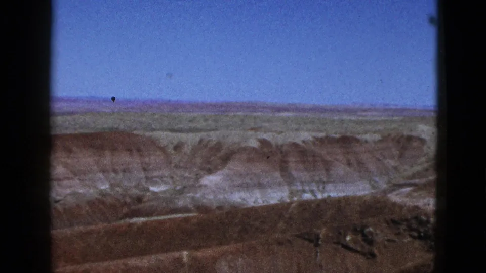 A 1953 California landscape frame with greenish plains, eroded mesa slopes, and dust specks from the 8mm scan.