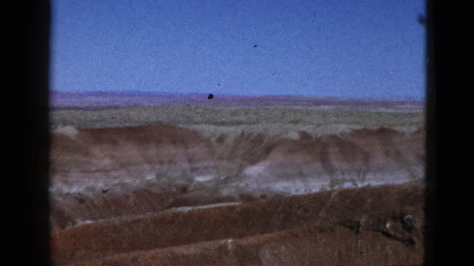 Final 1953 California 8mm frame looking over open fields toward brown mesas and pale eroded hills beneath blue sky.