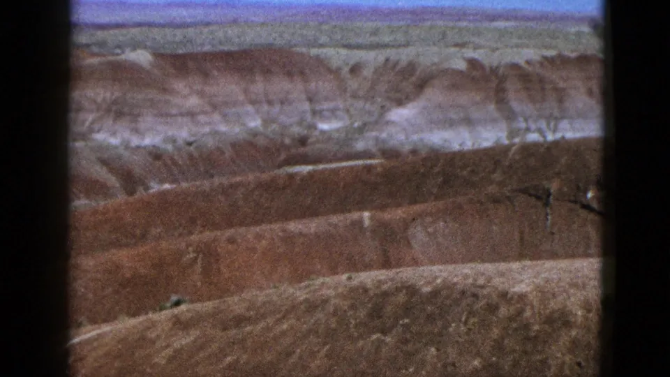 1953 California 8mm frame with a wide view of eroded red canyon slopes and pale rock layers.