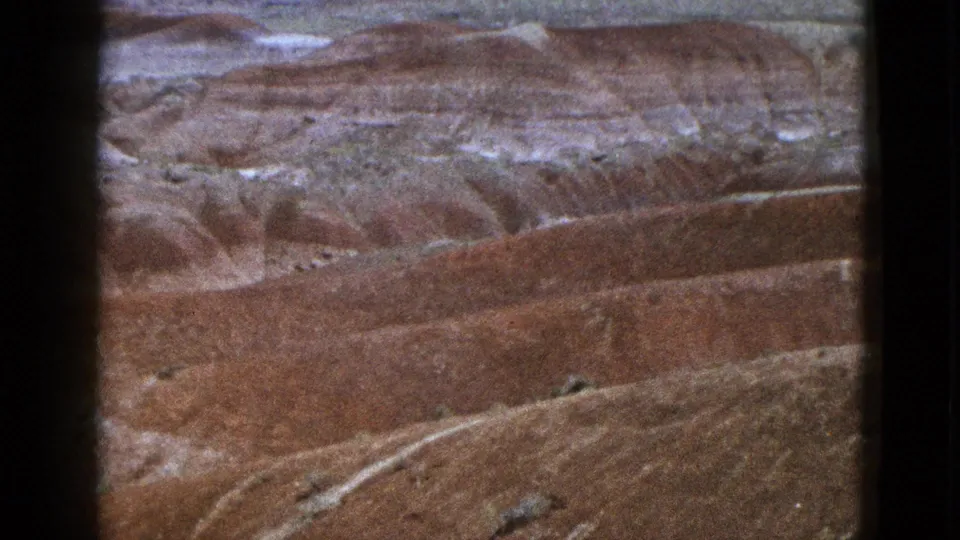 1953 California 8mm frame with red desert canyon ridges, light erosion bands, and sparse vegetation.