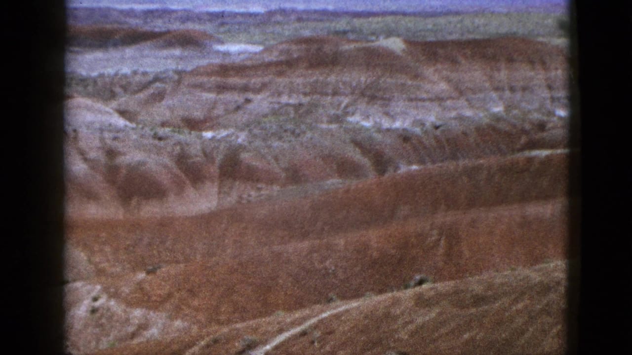 1953 California home-movie frame showing a broad desert canyon overlook with striated rock layers and distant horizon.