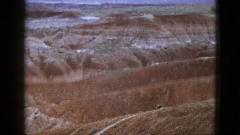1953 California home-movie frame showing a broad desert canyon overlook with striated rock layers and distant horizon.