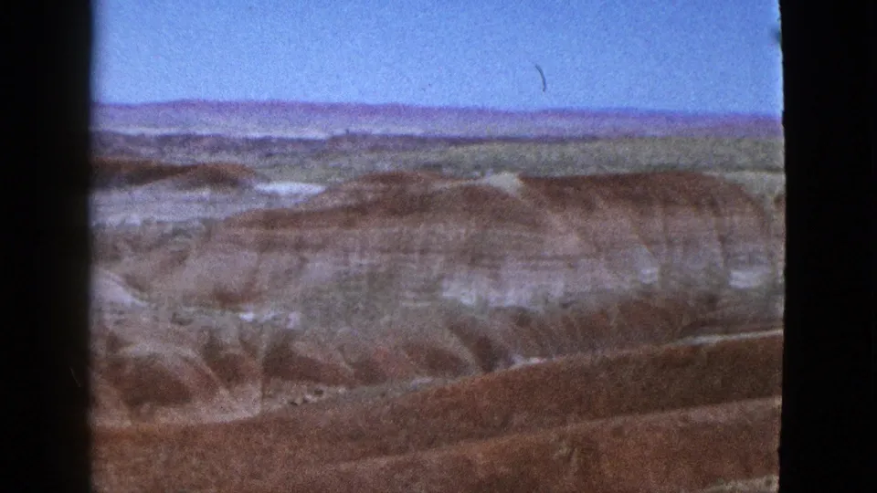 1953 California 8mm travel footage frame of eroded canyon ridges, pale gullies, and reddish-brown rock layers.
