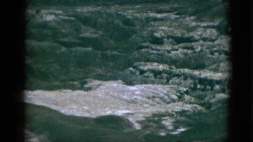 1953 California 8mm frame with darker exposure on rocky canyon ledges, pale eroded ground, and uneven terrain.