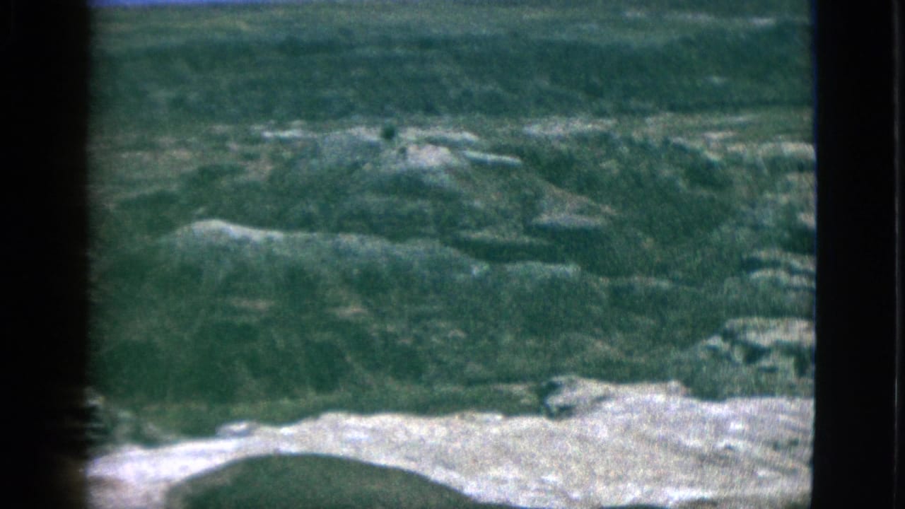 Wide view of rugged hills with a pale foreground slope and dark frame edges.