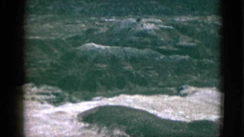 Soft 1953 California 8mm view of rolling hillside ridges and pale ground, framed by film-gate shadows.