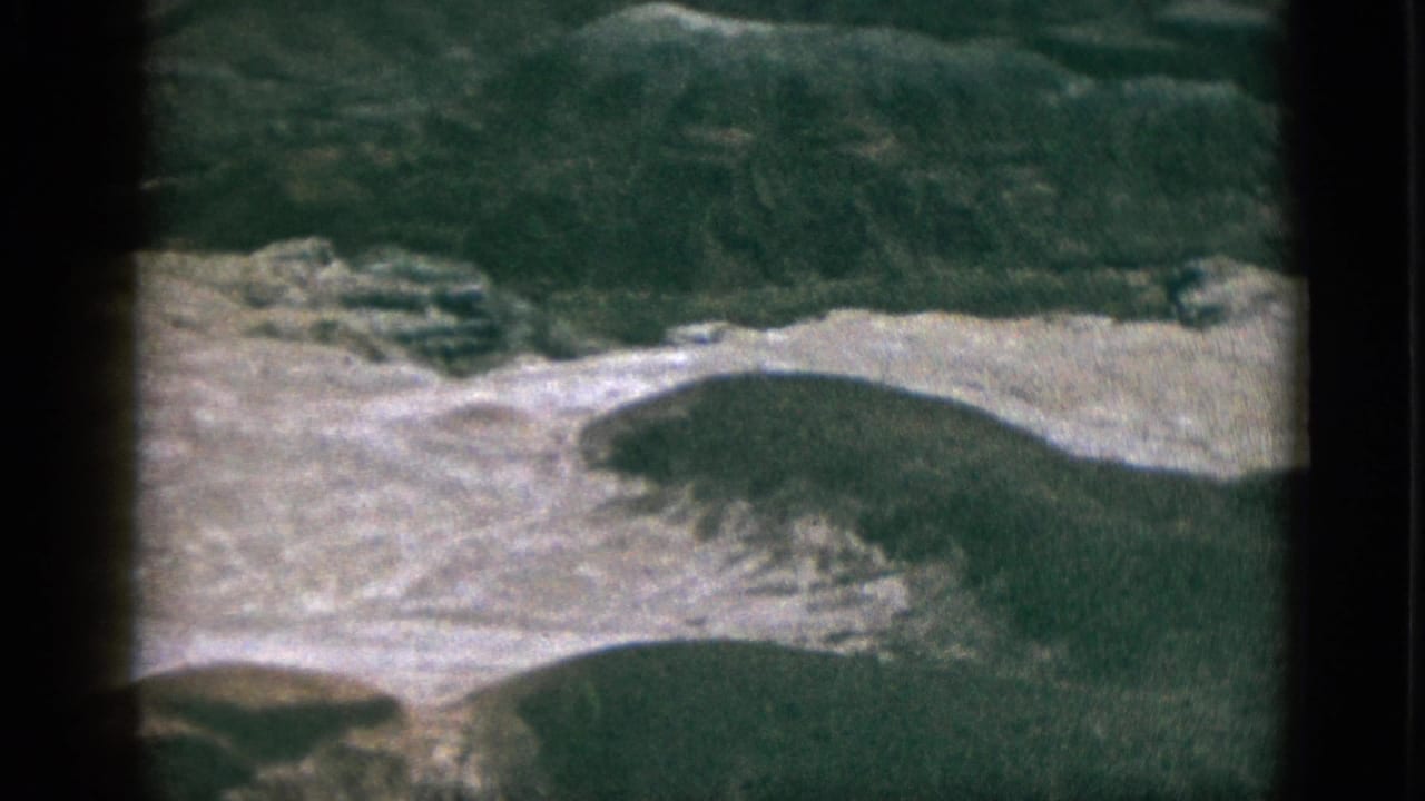 Aerial view of green hills and pale rocky slopes, seen through dark film-frame edges.