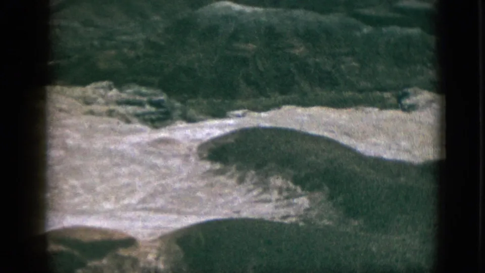 1953 California 8mm frame showing rolling green terrain and light rocky hillside from a high moving vantage.