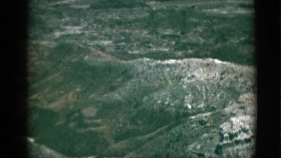 1953 California 8mm frame showing a green mountain slope with light rocky outcrops and soft archival color.