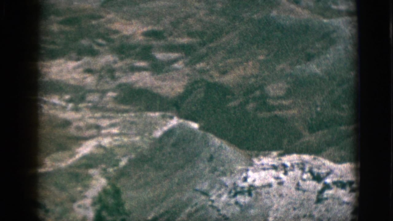 1953 8mm California frame shows rugged plateau hills and pale rock formations under a muted, grainy color image.