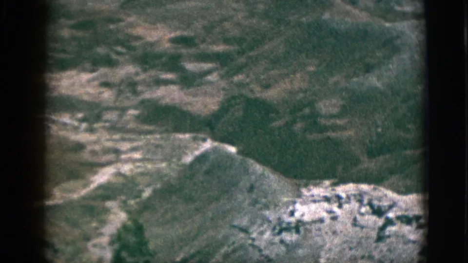 1953 8mm California frame shows rugged plateau hills and pale rock formations under a muted, grainy color image.