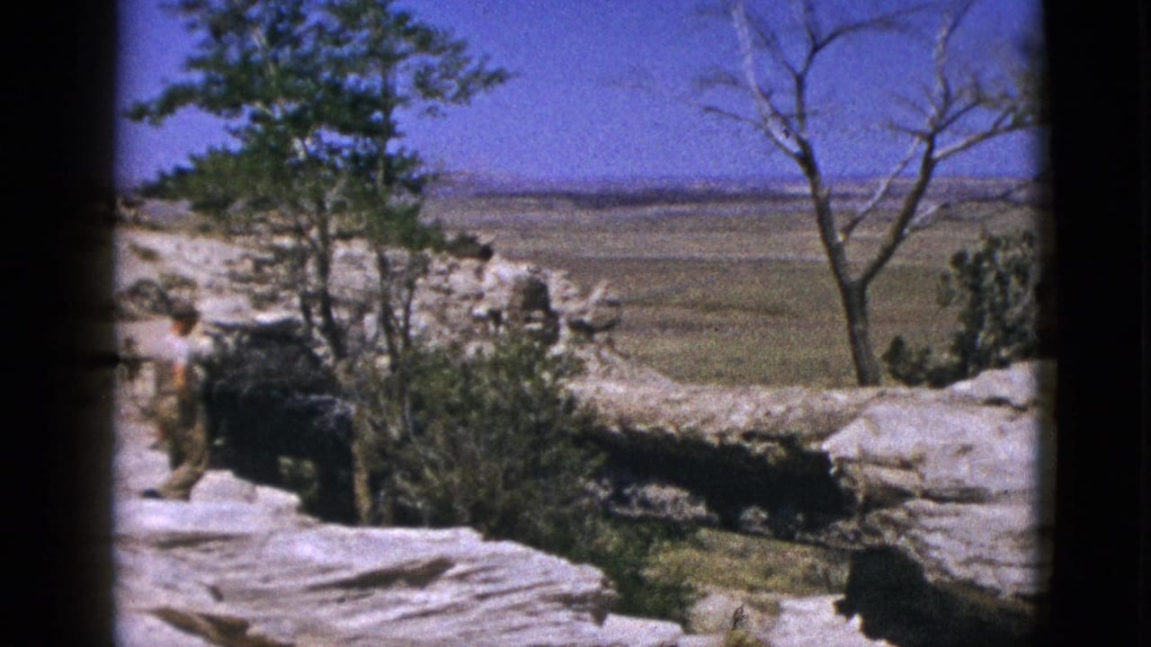 1953 California 8mm frame showing a rocky desert overlook, sparse trees, open horizon, and a distant person walking along the ledge.