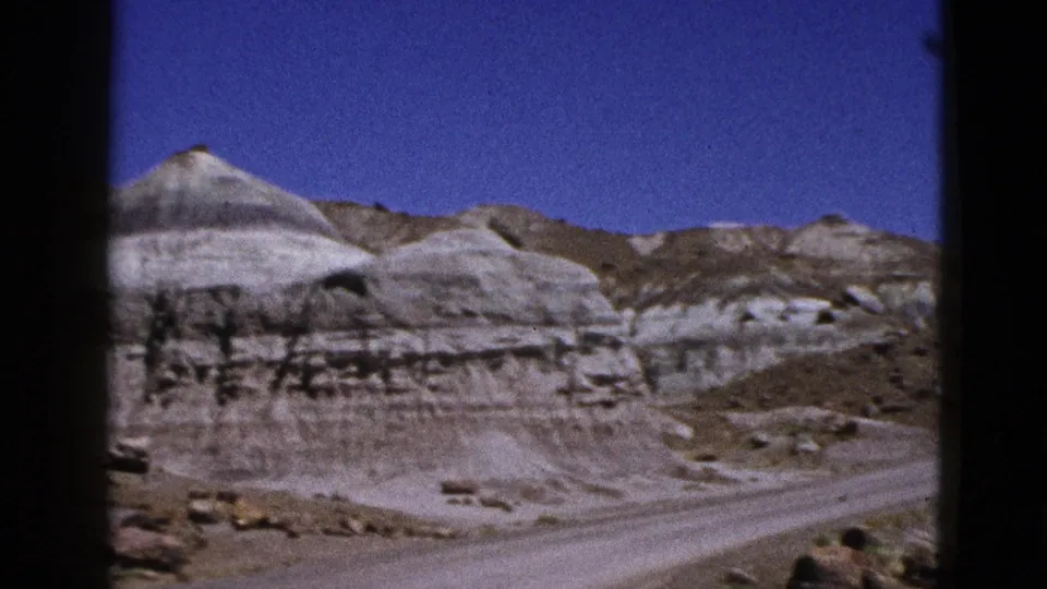 1953 California desert landscape with pale mineral-streaked formations, rough brown slopes, and a clear blue sky.
