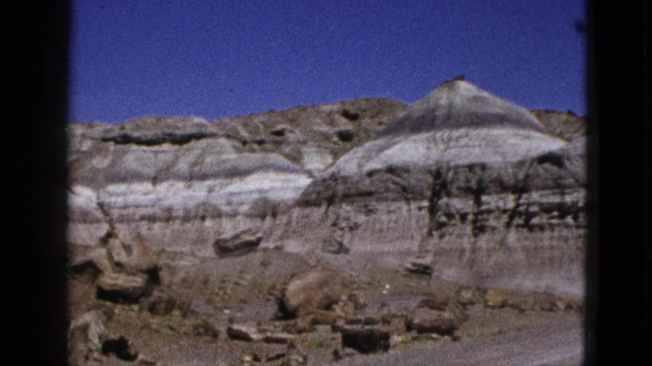 Sunlit layered rock formations with scattered boulders below a blue sky.
