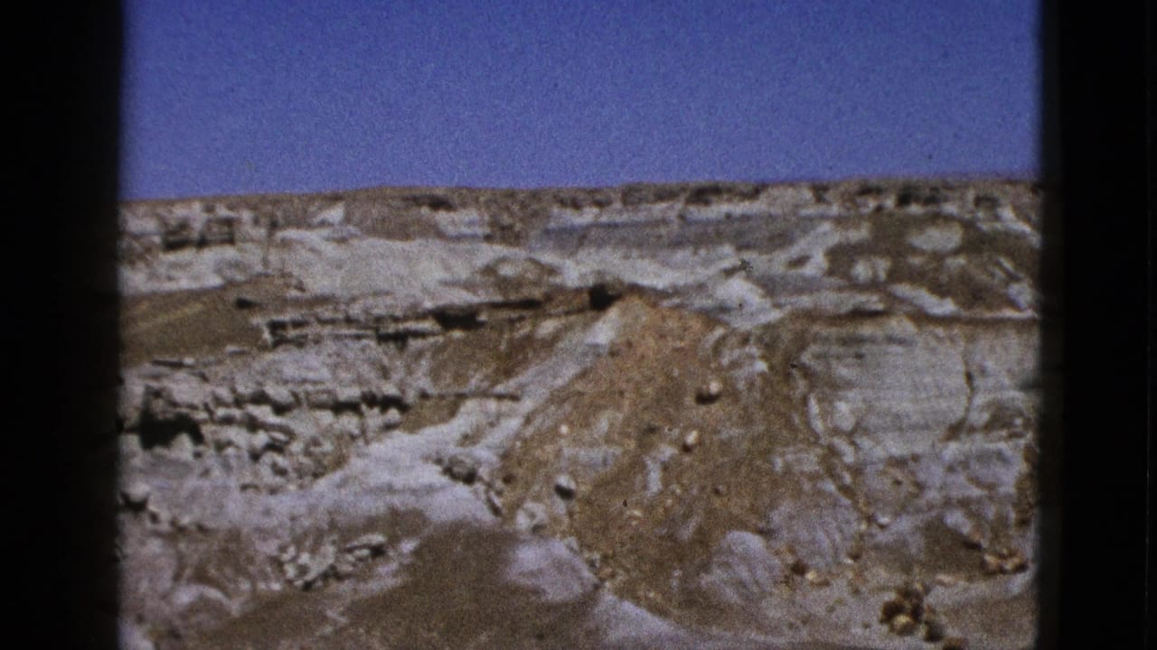 1953 California 8mm frame showing pale layered desert rock and a brown eroded mound beneath a clear blue sky.