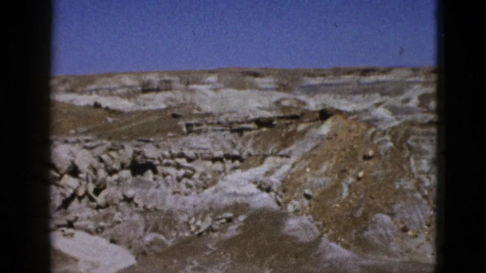 1953 California home-movie frame with multitone rocky desert formations, a rounded mound, and soft 8mm grain.