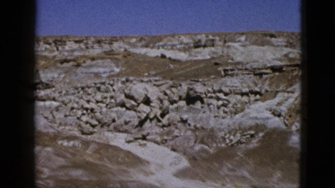 Wide canyon view with layered rock, boulders, dry washes, and blue sky.